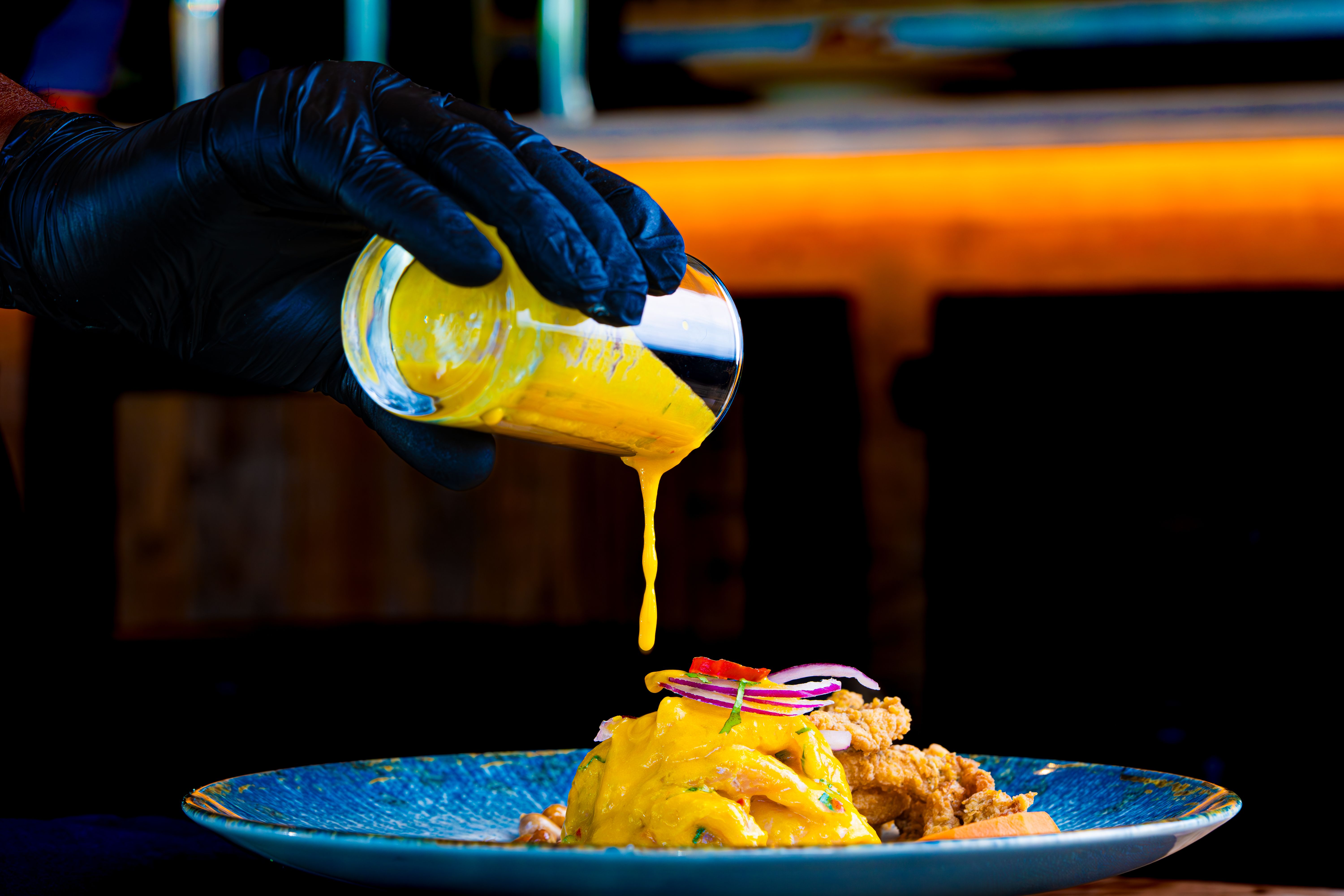 Chef adding vibrant yellow sauce to a plated gourmet dish